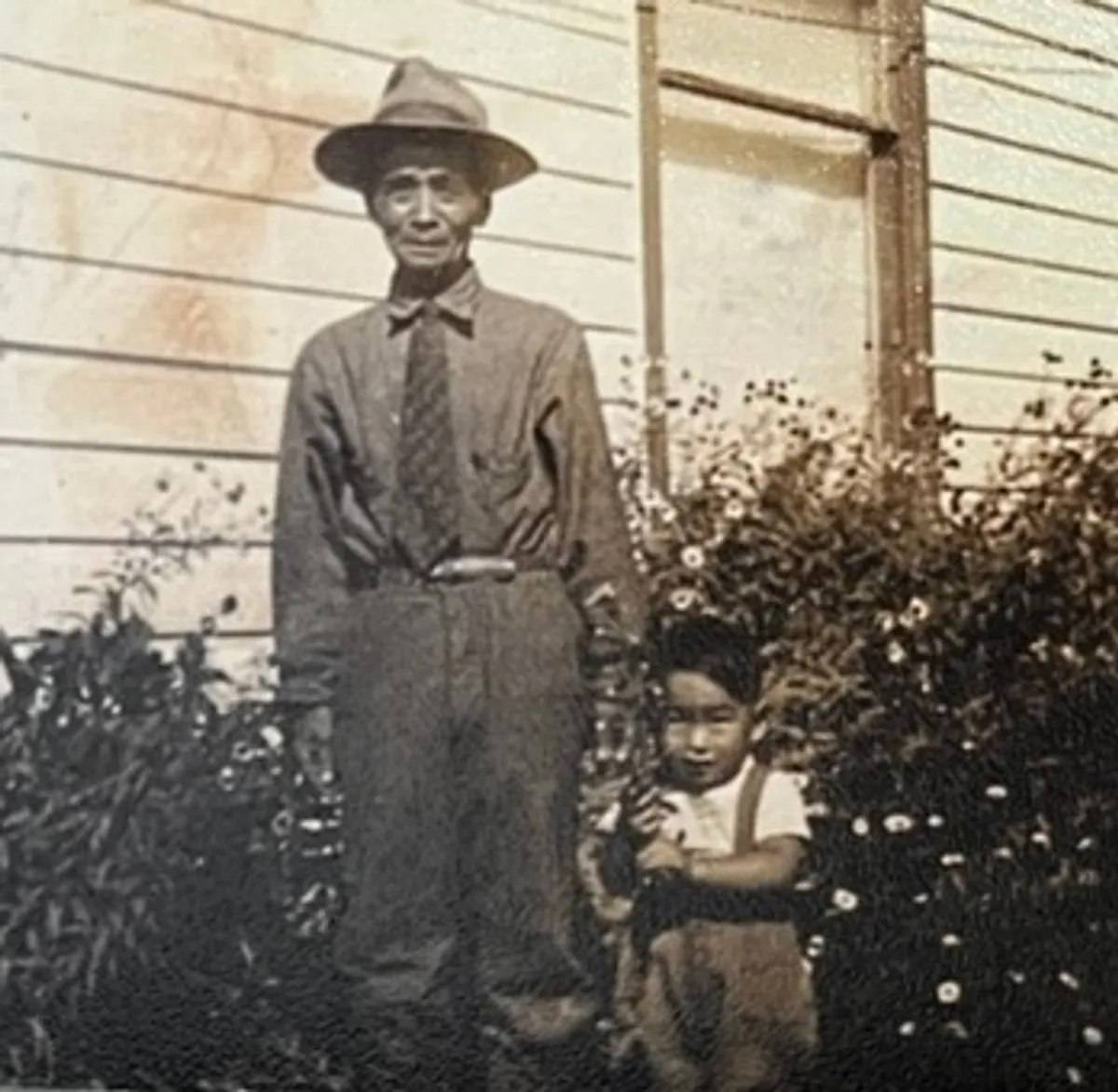 Before: water-stained snapshot of a man in a hat and a young boy beside a house