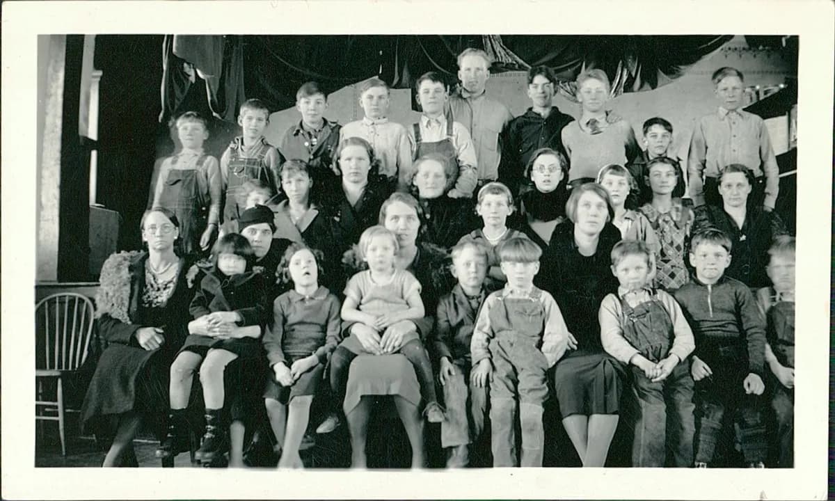 Before: black-and-white group photo of a large class of children and adults on a stage