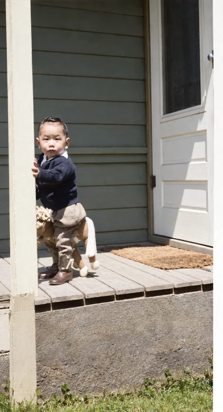 Restored: toddler in a navy sweater on a toy horse on a porch beside a white door
